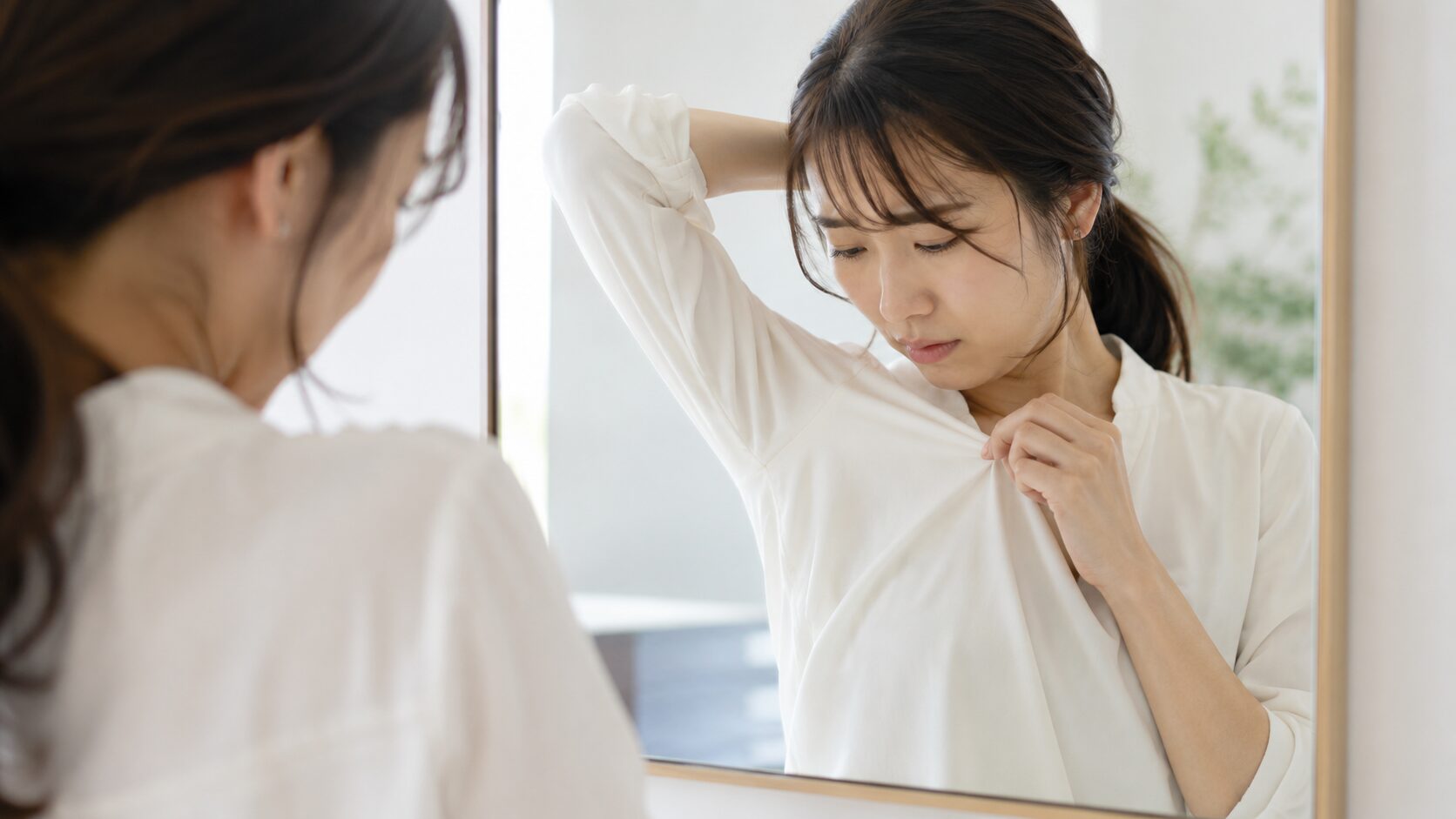 鏡の前で脇のニオイを気にする不安顔の女性
