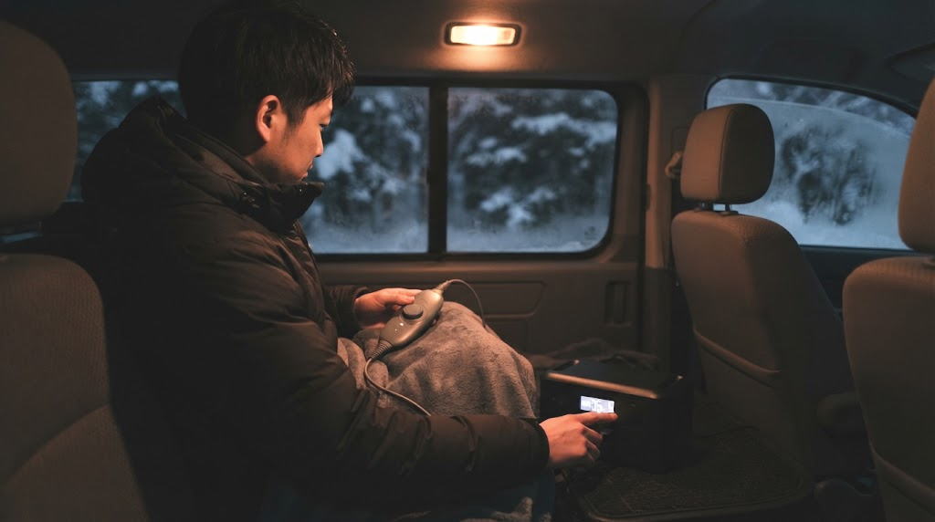 冬の車内で電気毛布とポータブル電源の残量を手元で確認する男性